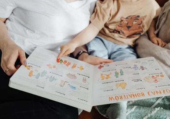 A mother and her son enjoy reading a children's book together while sitting on a cozy couch.
